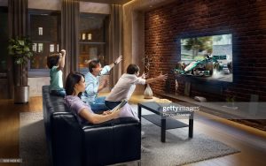 :biggrin:Father and two young children cheering and watching Sports Car Race on TV. Mother is reading a magazine. They are sitting on a sofa in the modern living room. The TV set is on the loft brick wall. It is evening outside the window. The car is artificial and made in 3D.